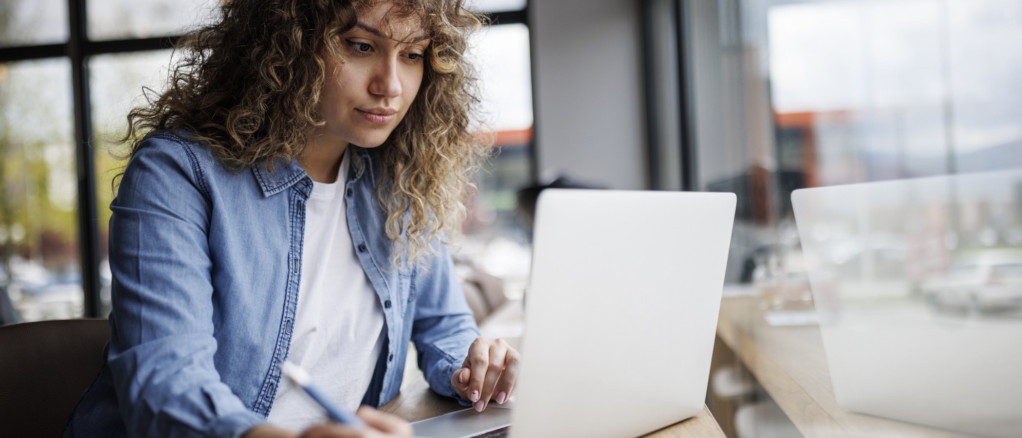 A consultant working at a laptop in a café, taking notes — side-on, natural daylight